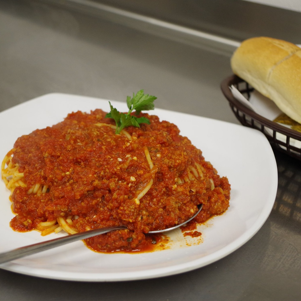 Spaghetti with rich red meat sauce and parsley garnish, served with a breadstick.
