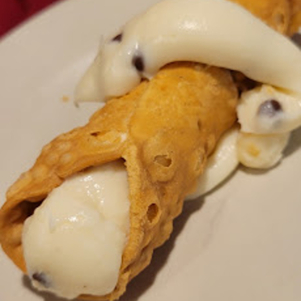 Two Coppola's cannolis, one filled with white cream and chocolate chips, on a white plate.