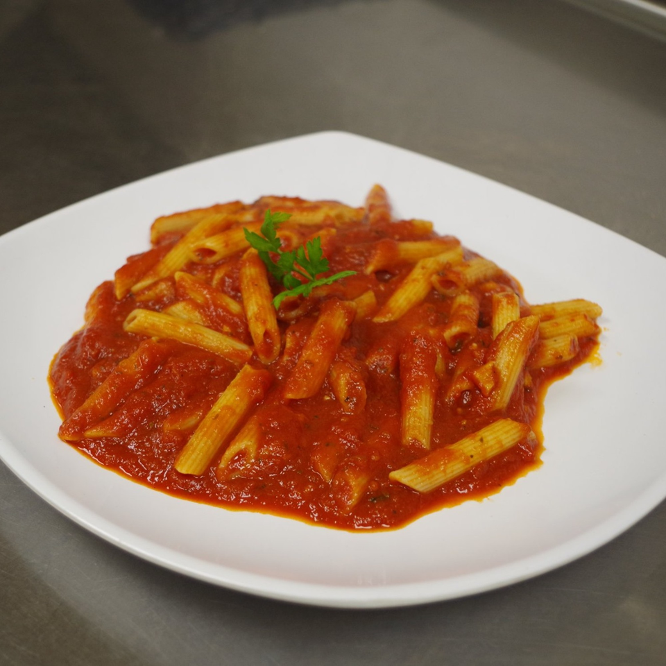 Penne pasta with rich red marinara sauce and a sprig of parsley on a white plate.